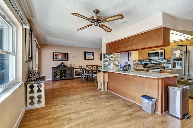 kitchen with decorative backsplash, brown cabinets, a peninsula, stainless steel appliances, and light wood-type flooring