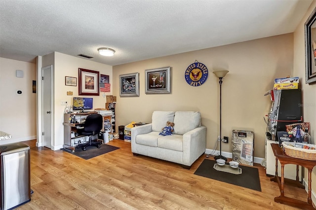 home office with a textured ceiling, light wood-type flooring, visible vents, and baseboards