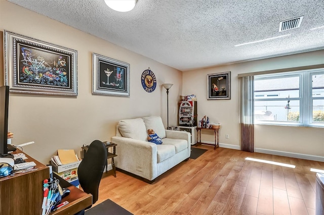 office space featuring light wood-type flooring, visible vents, a textured ceiling, and baseboards