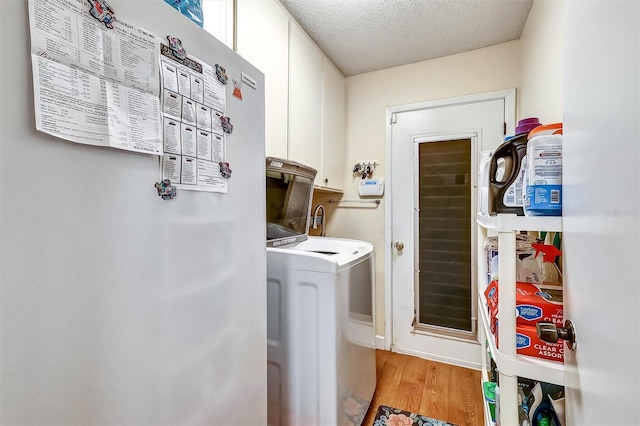 laundry room featuring washer and clothes dryer, cabinet space, a textured ceiling, and light wood finished floors