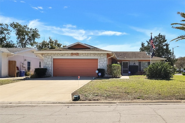 single story home featuring a front yard, stone siding, an attached garage, and concrete driveway