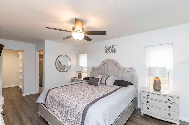 bedroom featuring ceiling fan, a spacious closet, baseboards, and dark wood-style flooring