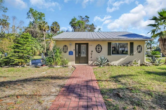 bungalow featuring stucco siding, metal roof, and a front lawn