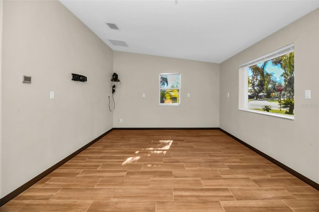 unfurnished room featuring lofted ceiling, baseboards, visible vents, and wood finish floors