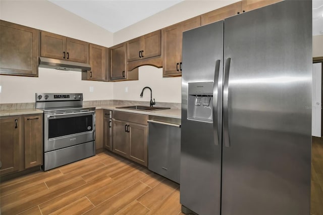 kitchen featuring wood tiled floor, under cabinet range hood, light countertops, stainless steel appliances, and a sink