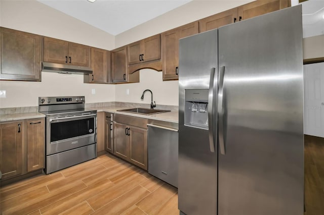 kitchen with wood finish floors, a sink, stainless steel appliances, light countertops, and under cabinet range hood