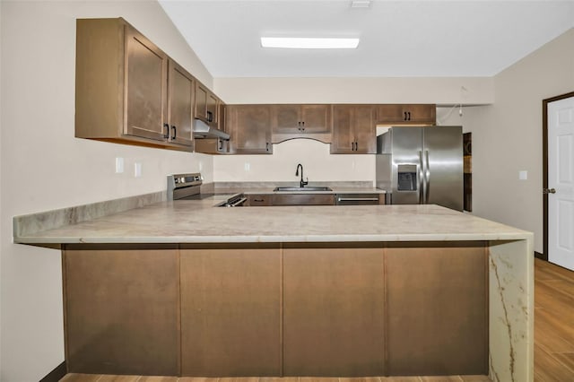 kitchen with a sink, under cabinet range hood, appliances with stainless steel finishes, a peninsula, and light countertops