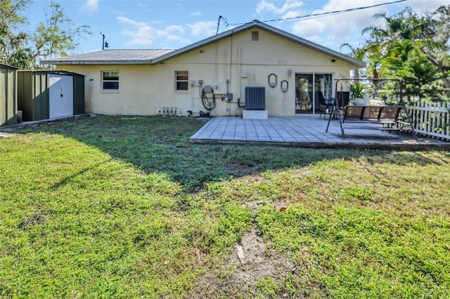 rear view of property featuring fence, a lawn, an outdoor structure, a patio area, and a storage unit