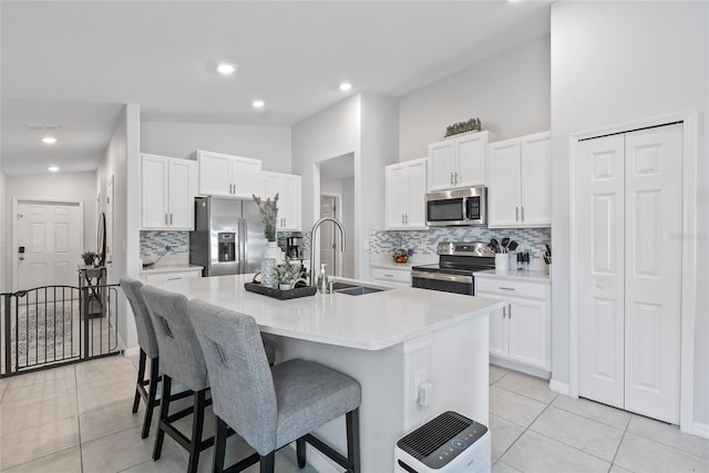 kitchen with a breakfast bar, a sink, white cabinetry, appliances with stainless steel finishes, and light tile patterned floors