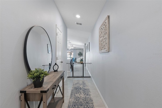 corridor with visible vents, baseboards, vaulted ceiling, light tile patterned floors, and an upstairs landing