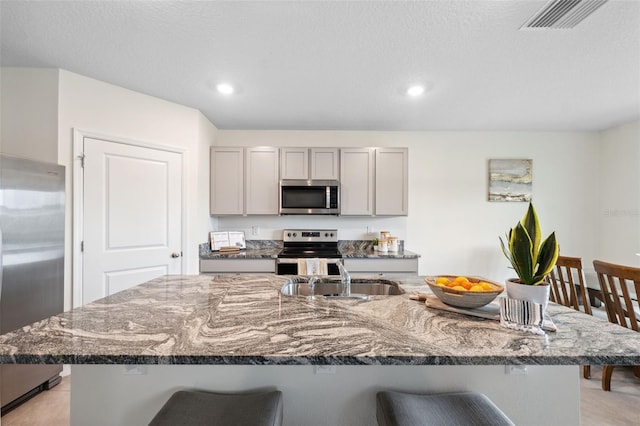 kitchen featuring appliances with stainless steel finishes, gray cabinets, a sink, and a breakfast bar area