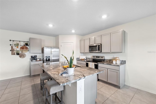 kitchen featuring appliances with stainless steel finishes, a kitchen bar, a sink, and gray cabinetry