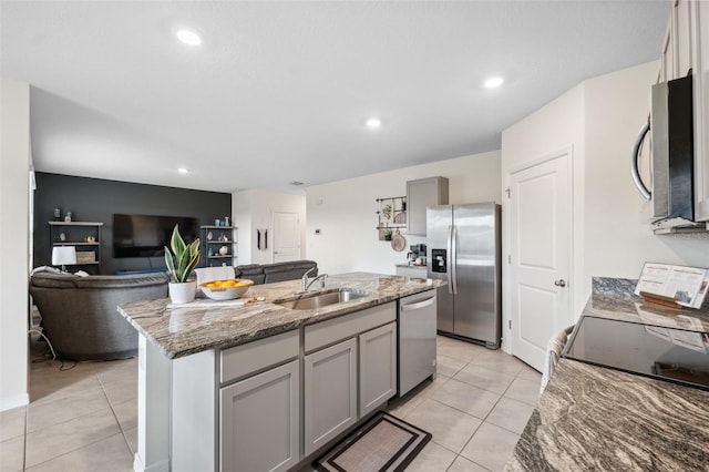 kitchen with appliances with stainless steel finishes, light stone countertops, a kitchen island with sink, gray cabinetry, and a sink