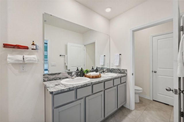 full bath featuring toilet, tile patterned flooring, double vanity, and a sink