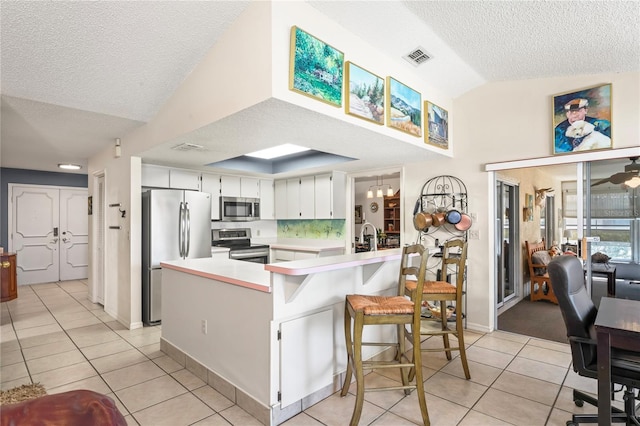 kitchen with light tile patterned floors, a peninsula, vaulted ceiling, stainless steel appliances, and light countertops