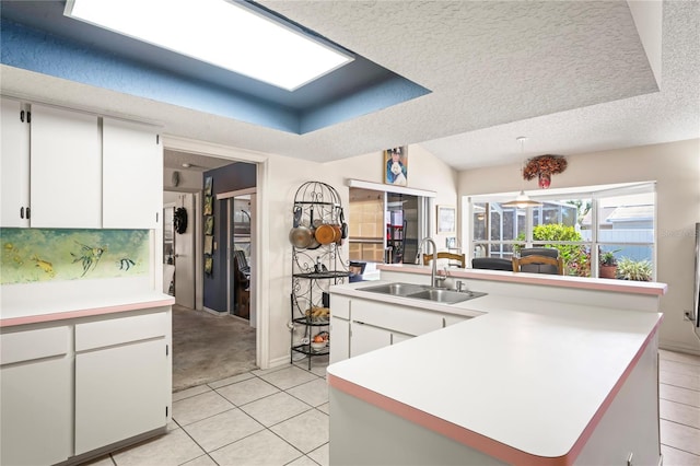 kitchen with a textured ceiling, light countertops, a tray ceiling, and a sink