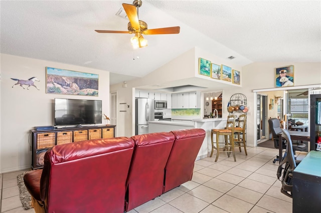 living area with a ceiling fan, lofted ceiling, visible vents, and light tile patterned floors