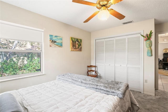 bedroom featuring a textured ceiling, ceiling fan, visible vents, a closet, and carpet