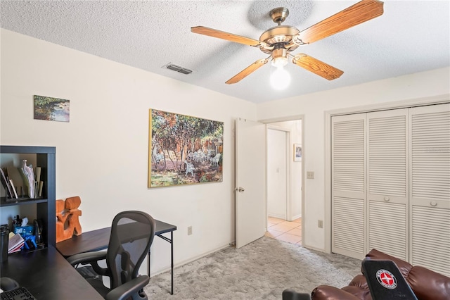 carpeted office space featuring visible vents, ceiling fan, and a textured ceiling