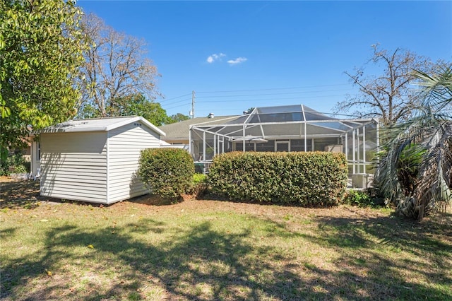 rear view of house with glass enclosure, a lawn, and an outdoor structure