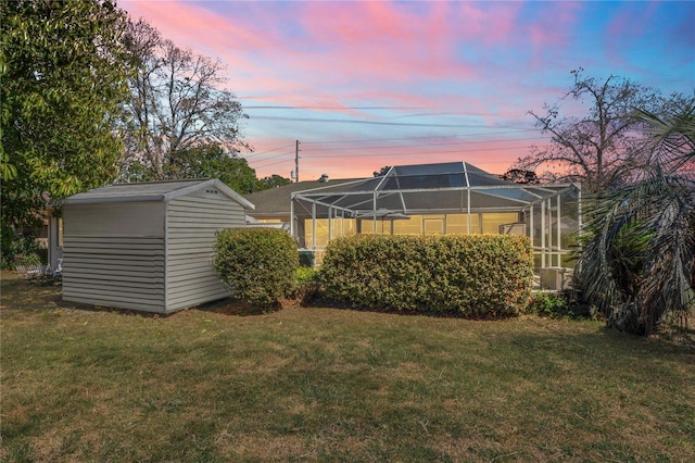 yard at dusk with a lanai, an outdoor structure, and a storage unit