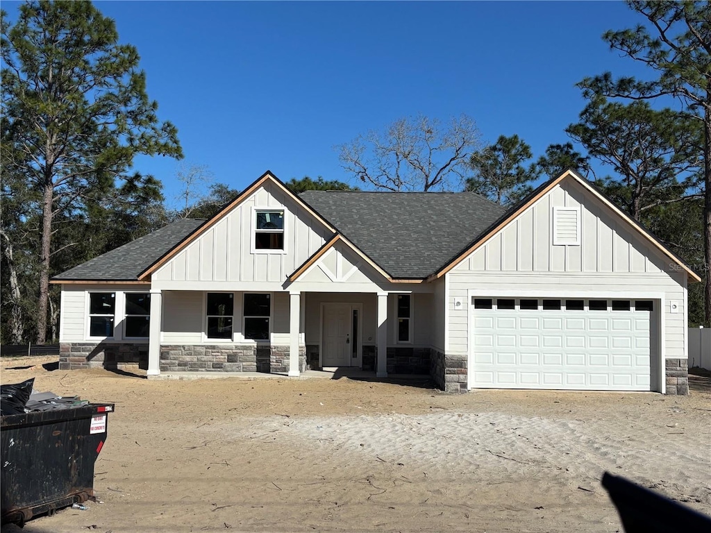 modern farmhouse style home with board and batten siding, stone siding, roof with shingles, and a garage