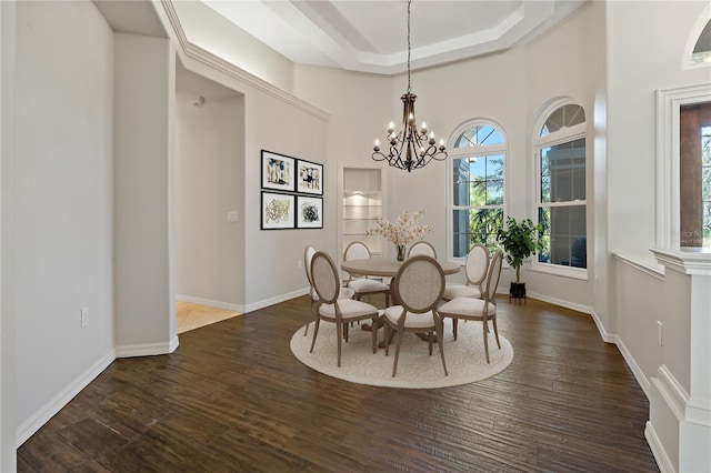dining space with a raised ceiling, a notable chandelier, a healthy amount of sunlight, and dark wood finished floors