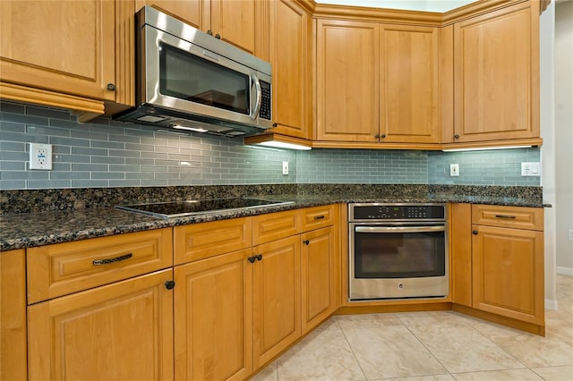 kitchen with light tile patterned floors, stainless steel appliances, backsplash, and dark stone counters