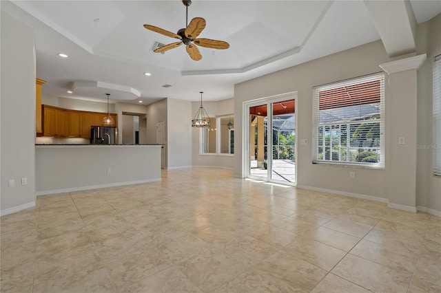unfurnished living room with a raised ceiling, ceiling fan with notable chandelier, recessed lighting, light tile patterned floors, and baseboards