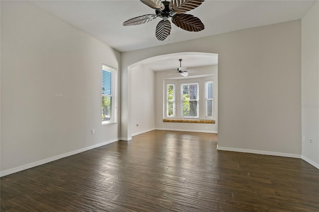 spare room with baseboards, arched walkways, dark wood-type flooring, and a ceiling fan