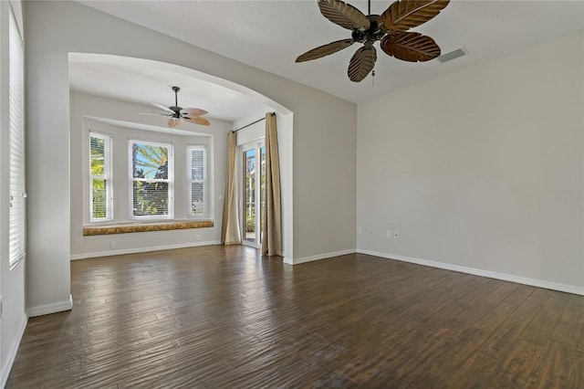 empty room featuring visible vents, arched walkways, baseboards, and dark wood finished floors