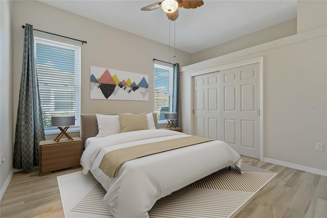 bedroom with a closet, light wood-style flooring, a ceiling fan, and baseboards