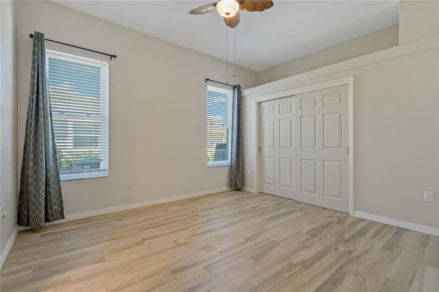 unfurnished bedroom with multiple windows, baseboards, light wood-type flooring, and a closet