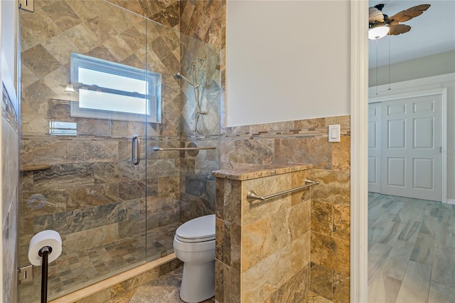 bathroom featuring toilet, tile walls, wainscoting, a shower stall, and ceiling fan