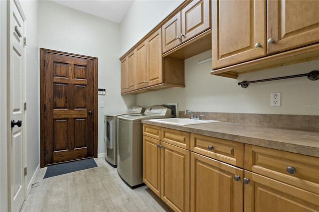 washroom featuring light wood-style flooring, a sink, washing machine and dryer, cabinet space, and baseboards
