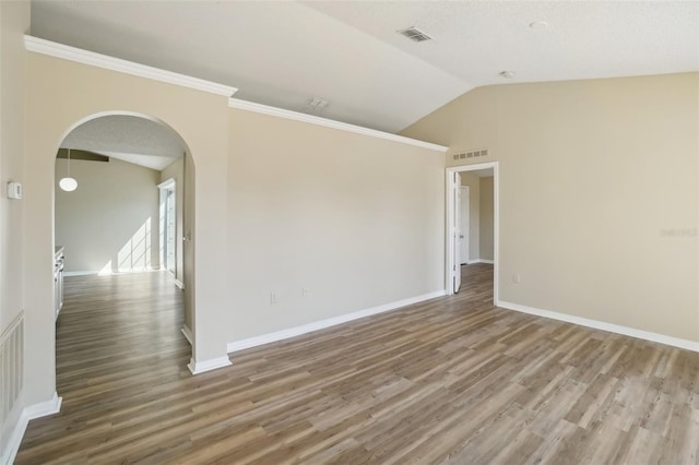 spare room featuring lofted ceiling, wood finished floors, arched walkways, and visible vents