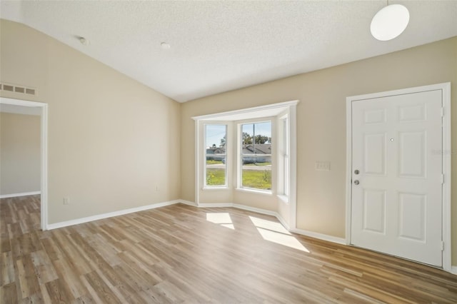 foyer featuring visible vents, vaulted ceiling, a textured ceiling, light wood-type flooring, and baseboards