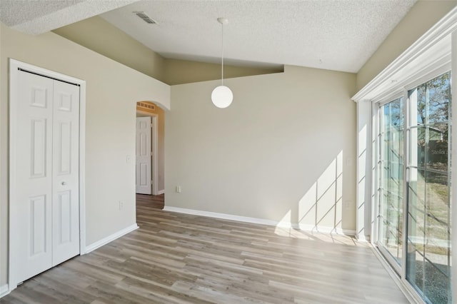 unfurnished dining area featuring lofted ceiling, visible vents, a textured ceiling, wood finished floors, and baseboards