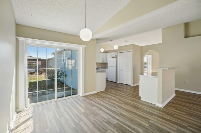 interior space featuring lofted ceiling, arched walkways, white cabinetry, freestanding refrigerator, and dark wood finished floors