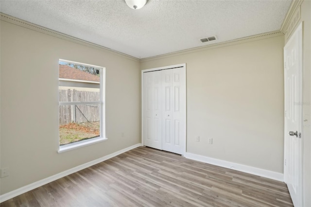 unfurnished bedroom featuring a textured ceiling, wood finished floors, visible vents, baseboards, and a closet