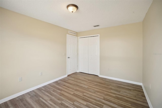 unfurnished bedroom with a closet, a textured ceiling, baseboards, and wood finished floors