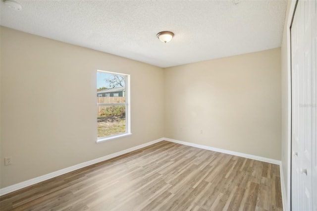 spare room with light wood-type flooring, baseboards, and a textured ceiling