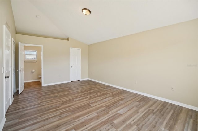 unfurnished bedroom with lofted ceiling, a closet, wood finished floors, and baseboards