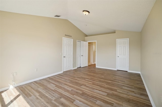 unfurnished bedroom with visible vents, vaulted ceiling, baseboards, and wood finished floors