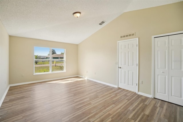 unfurnished bedroom with lofted ceiling, visible vents, a textured ceiling, and wood finished floors