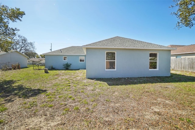 rear view of property with stucco siding, roof with shingles, fence, and a yard