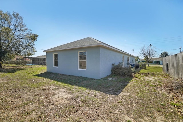 view of property exterior featuring a yard, fence, a shingled roof, and stucco siding