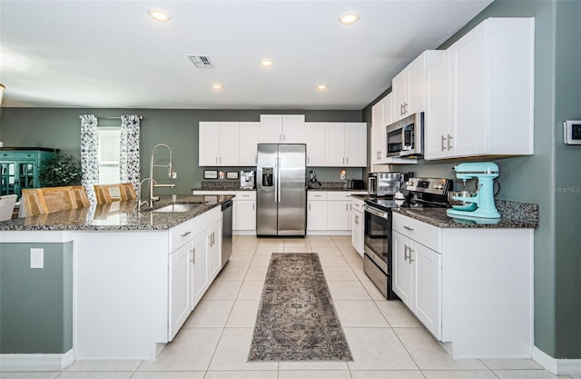 kitchen featuring stainless steel appliances, a sink, visible vents, white cabinets, and dark stone counters