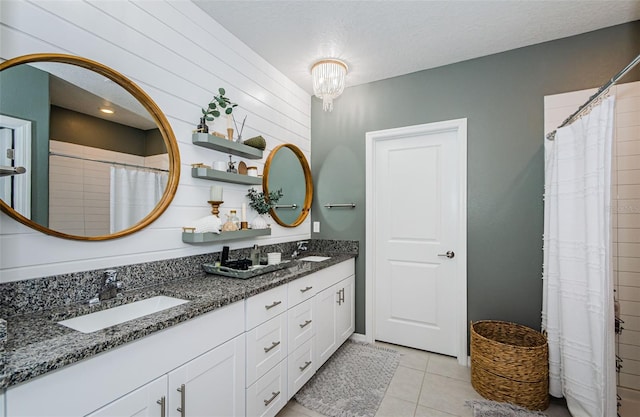 full bath with a textured ceiling, double vanity, a sink, and tile patterned floors