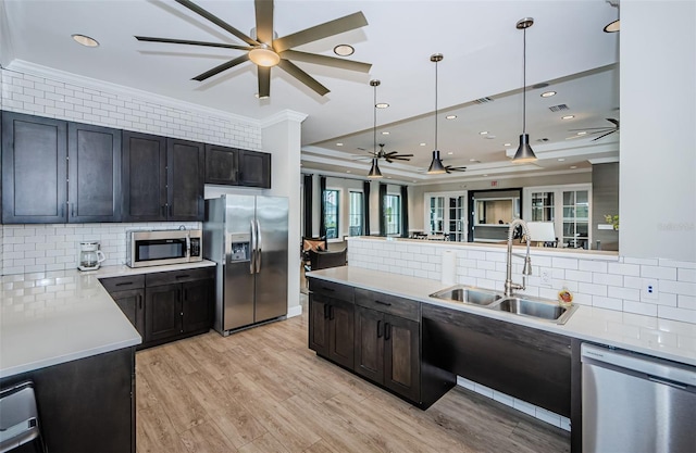 kitchen with light countertops, appliances with stainless steel finishes, light wood-style floors, ornamental molding, and a sink